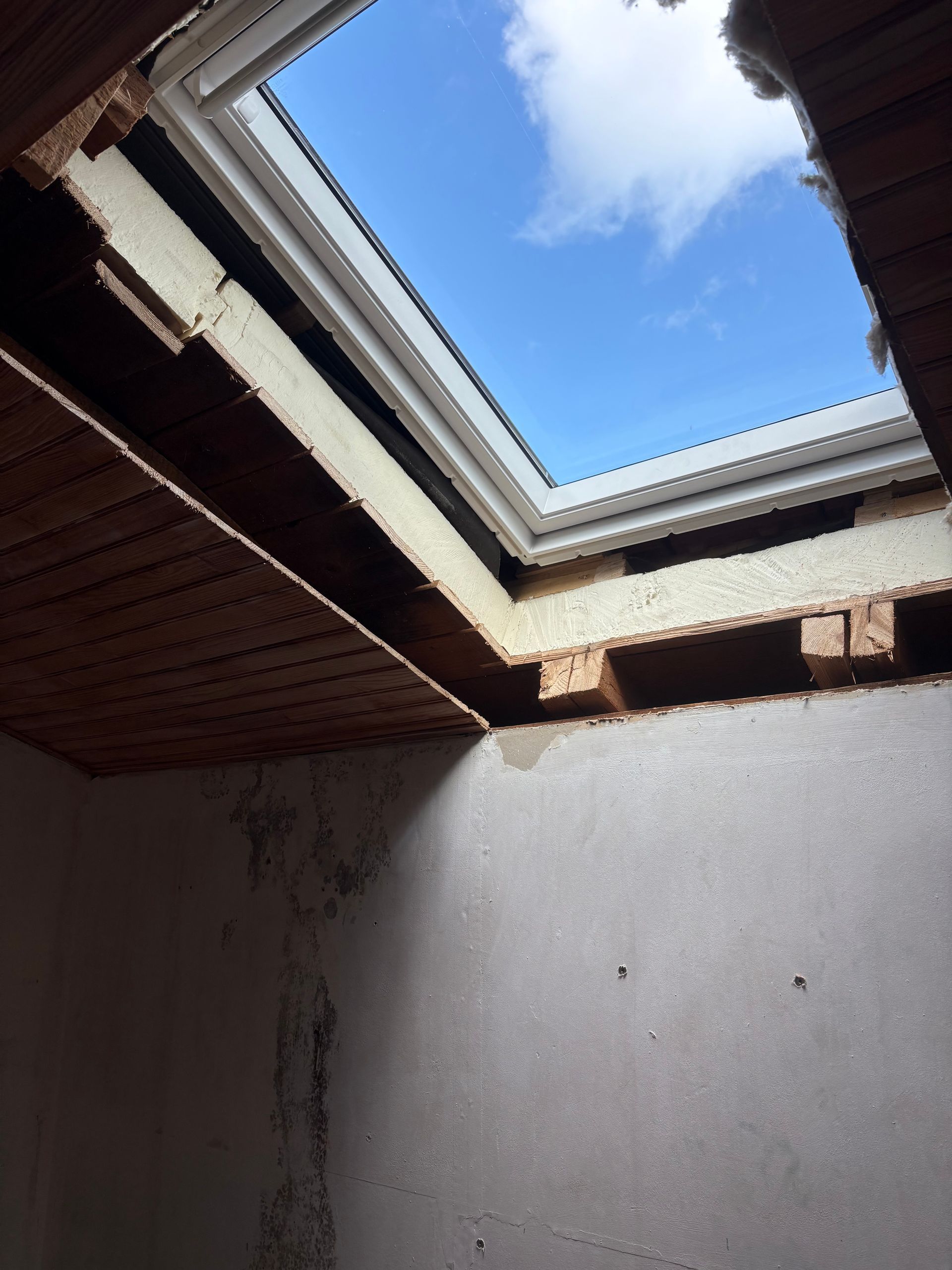 Vue depuis une pièce avec puits de lumière. Ciel d'un bleu éclatant visible. Poutres et mur du plafond apparents.