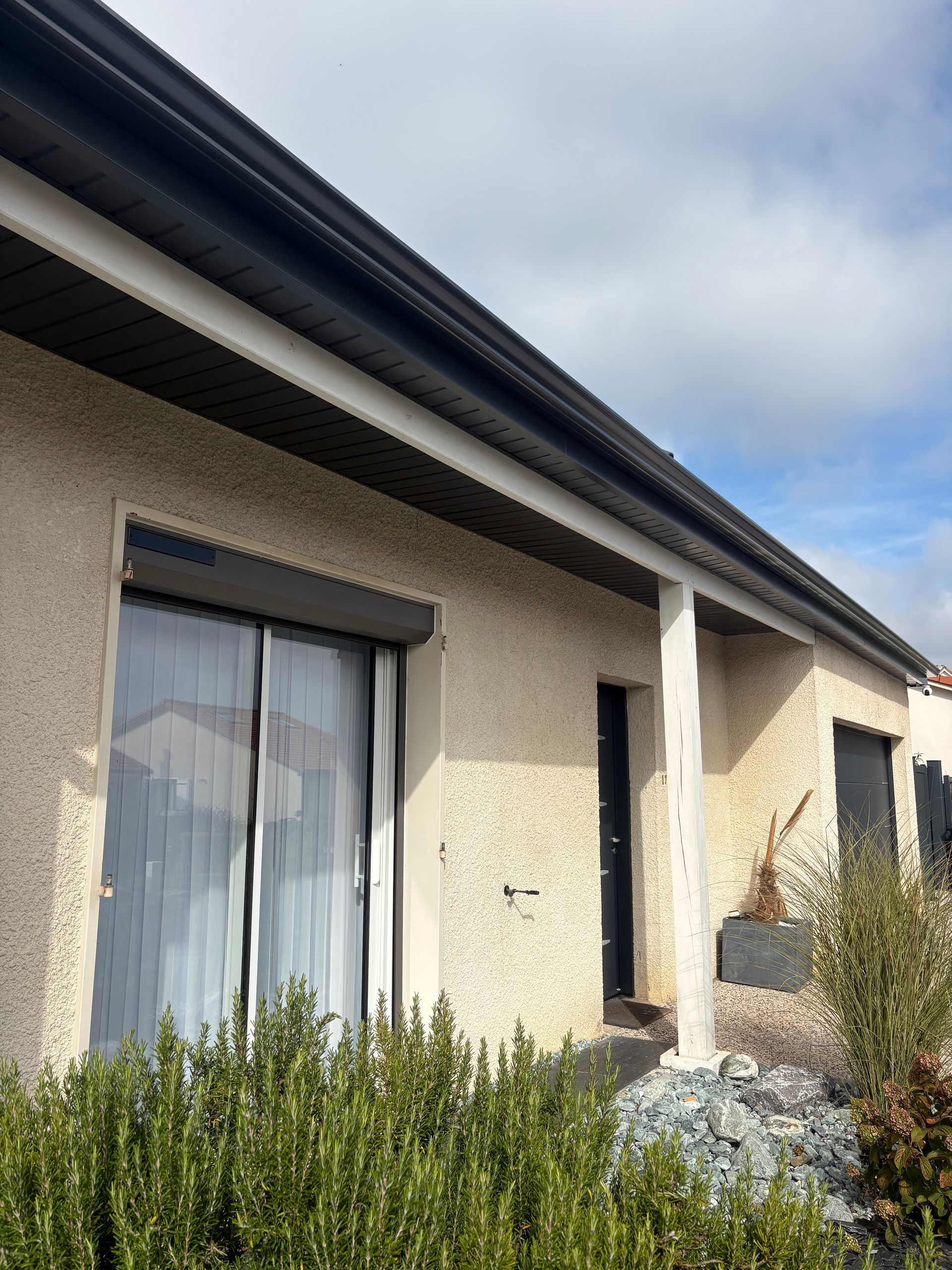 Maison en stuc beige avec toit et rideaux foncés ; porte sous un porche d'entrée.