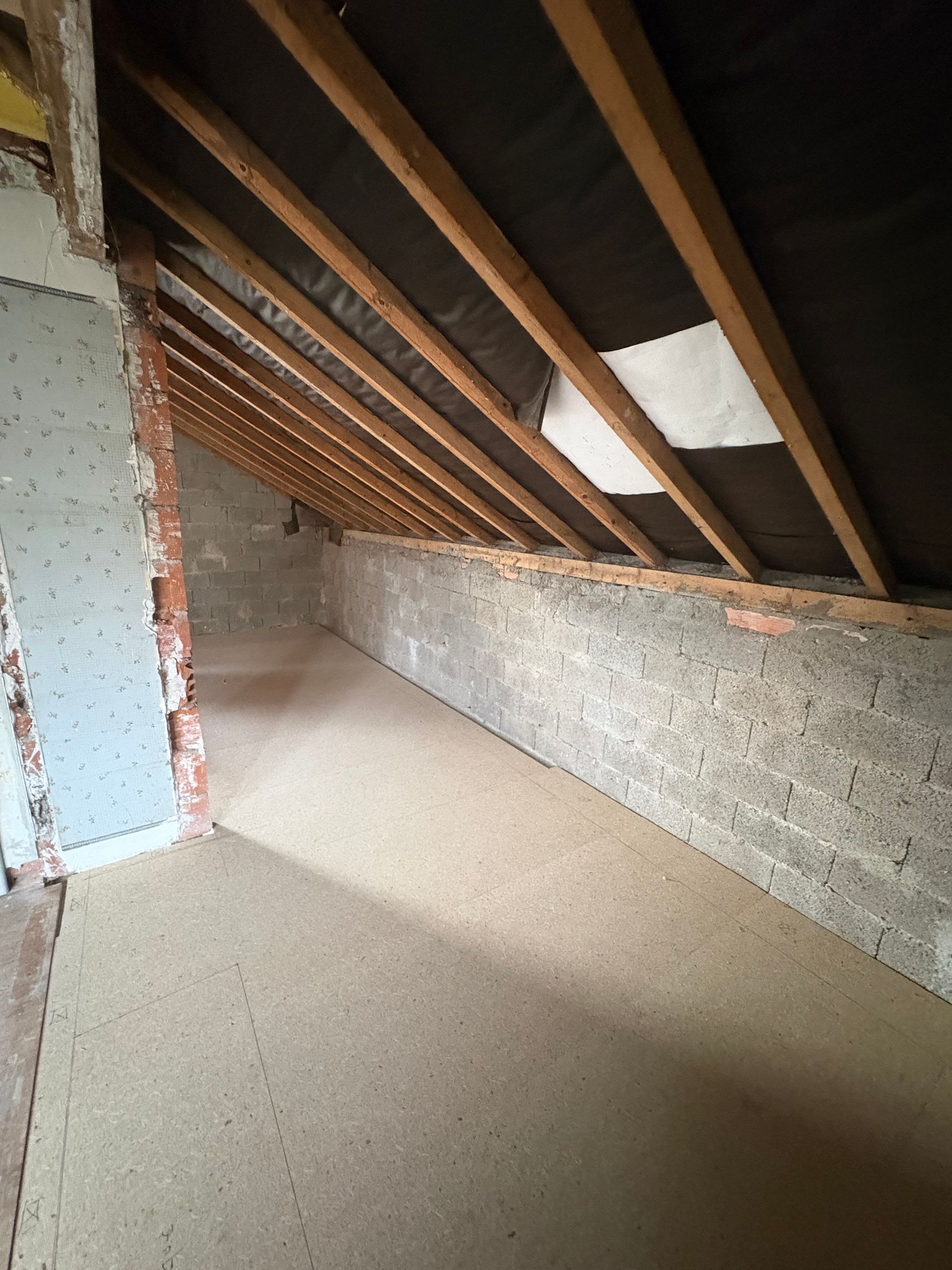 Aménagement des combles : poutres en bois, murs en briques et parpaings et sol en liège.