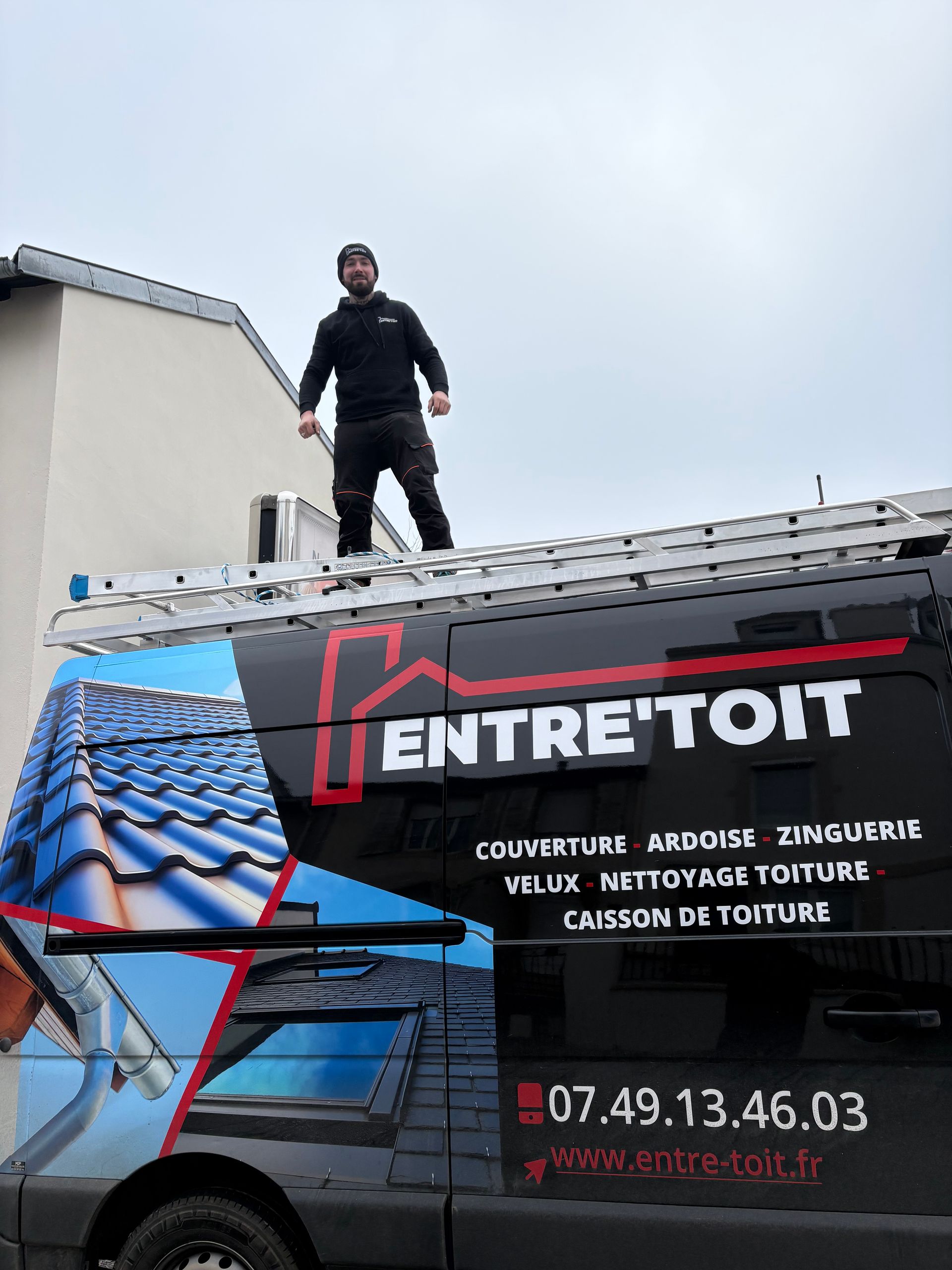 Un homme se tient sur un toit, au-dessus d'une camionnette avec le logo Entretoit.