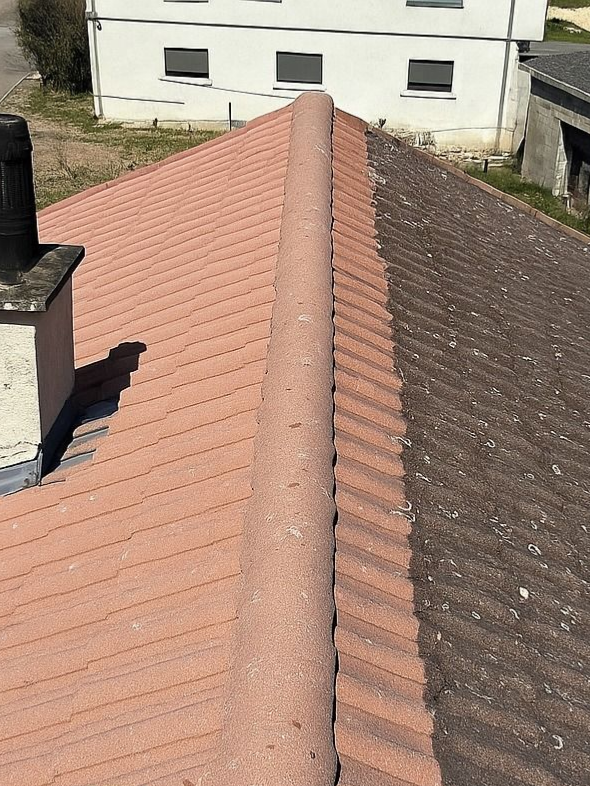 Toiture en tuiles rouges et brunes avec une arête centrale, présentant un contraste de couleur et de texture.