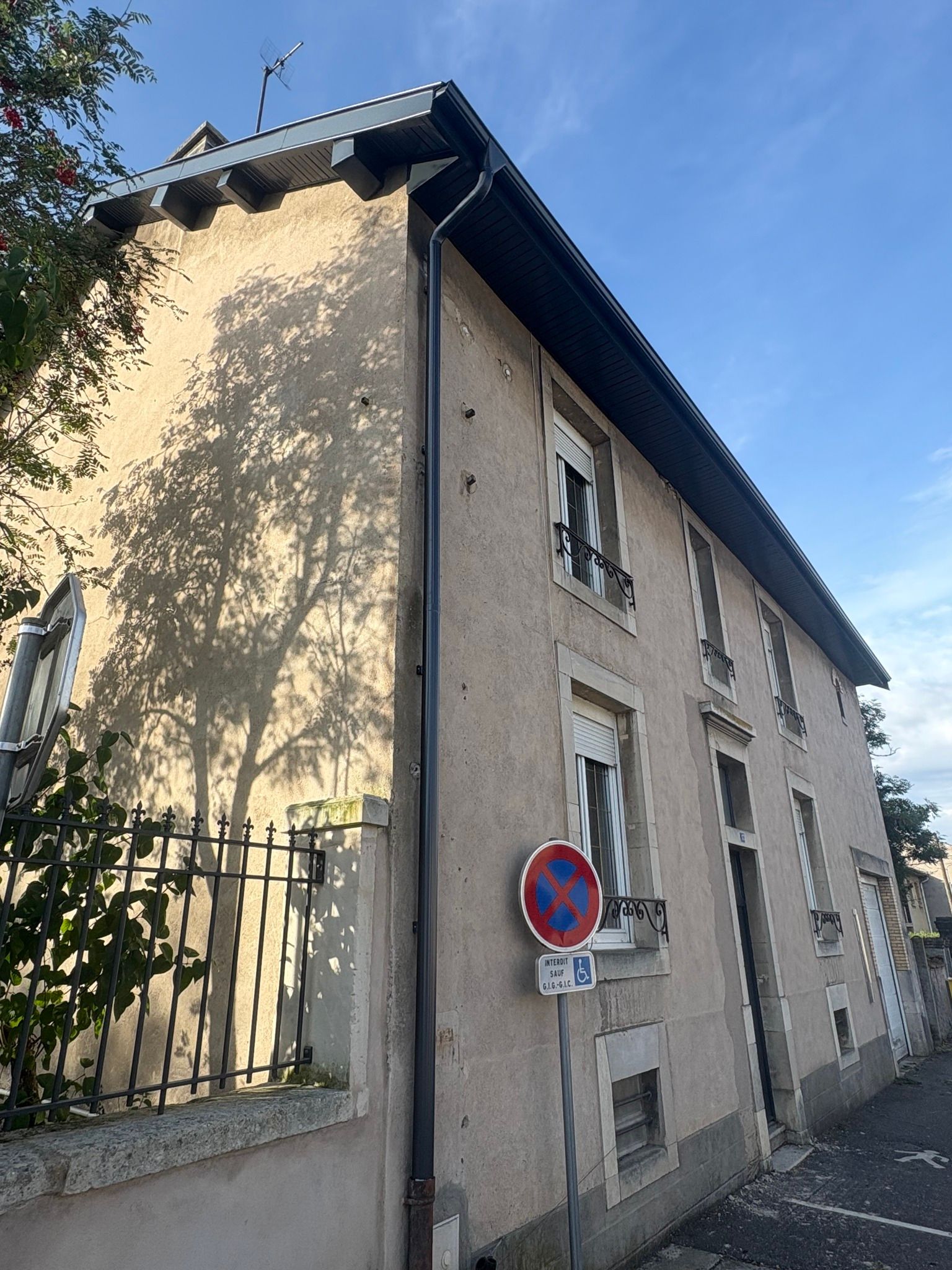 Bâtiment beige à étages avec toit et fenêtres foncés, clôture métallique noire et panneau Stationnement interdit.