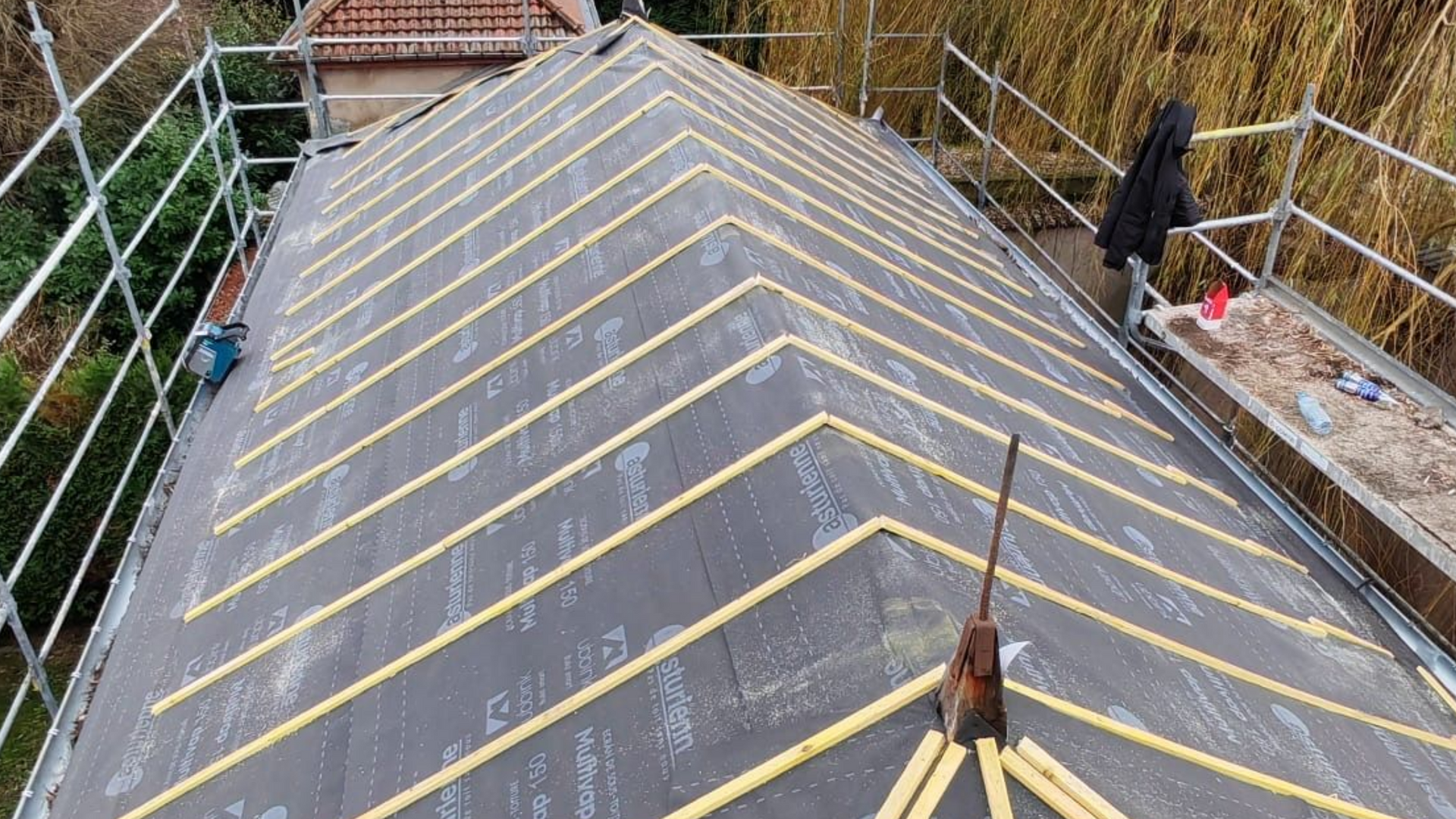 Vue d'un toit avec isolation extérieure, des échafaudages et un bâtiment partiellement visible.