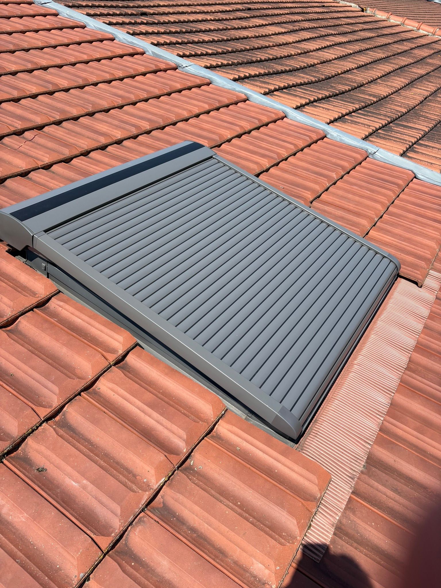 Aérateur de toit gris installé sur un toit de tuiles rouges.