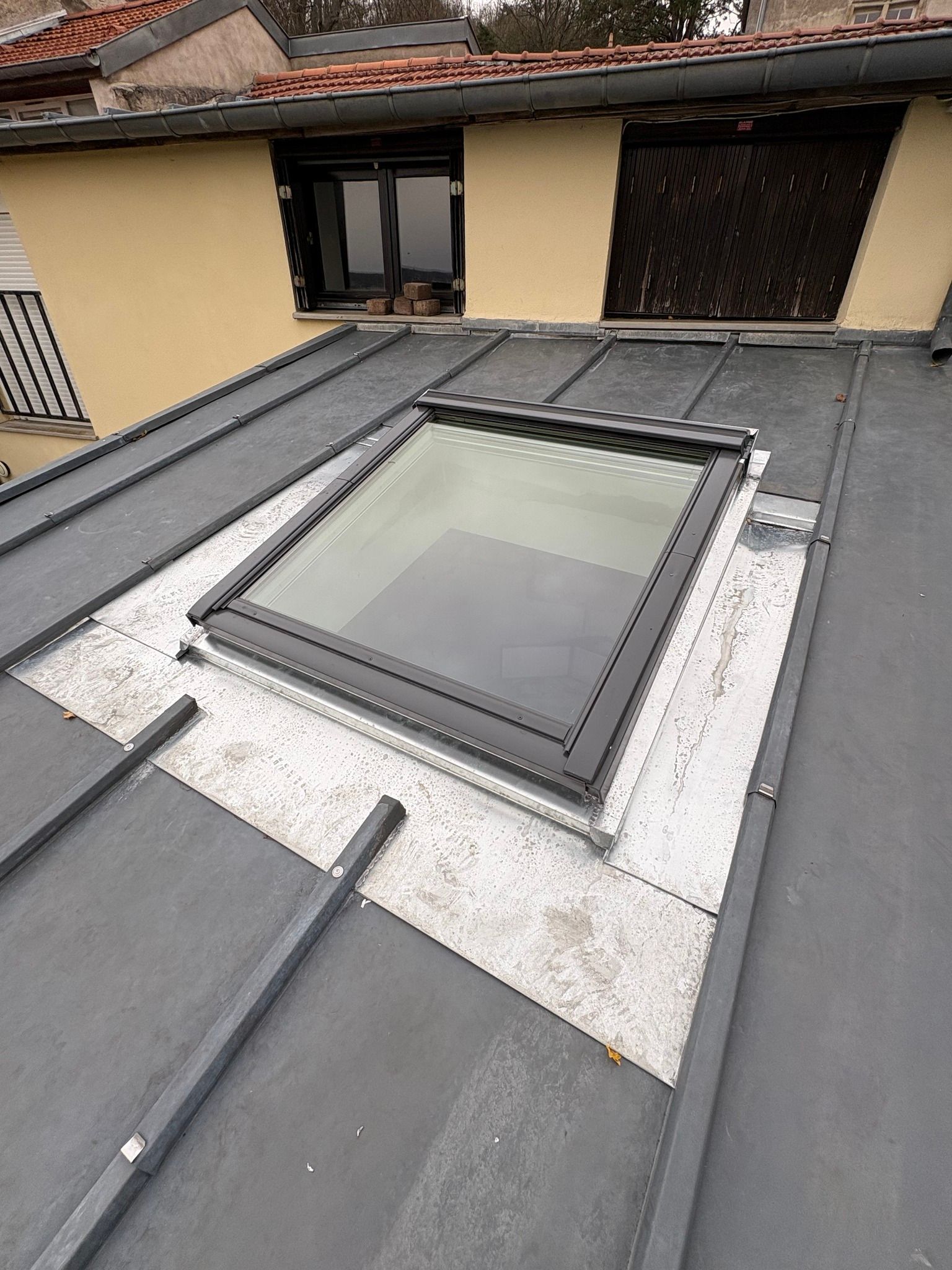Toiture avec un puits de lumière rectangulaire et costière en zinc.