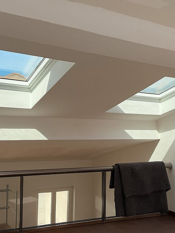 Vue intérieure avec puits de lumière, rambarde et couverture. La lumière du soleil illumine les murs blancs.