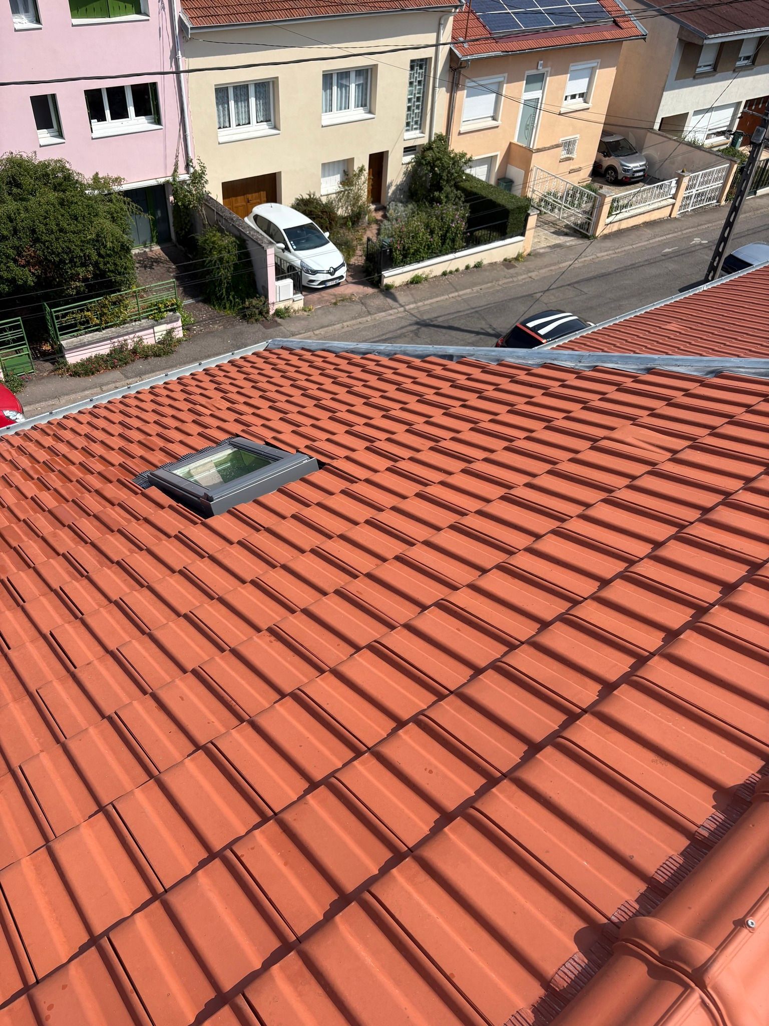 Toit en tuiles de terre cuite avec un puits de lumière ; rue et maisons en arrière-plan.