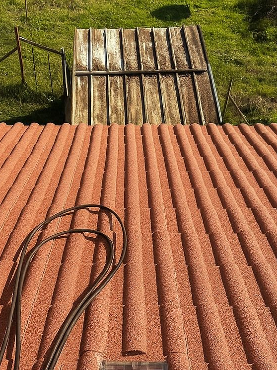Toit en tôle ondulée rouge avec une porte métallique et un câble noir. Herbe verte en arrière-plan.