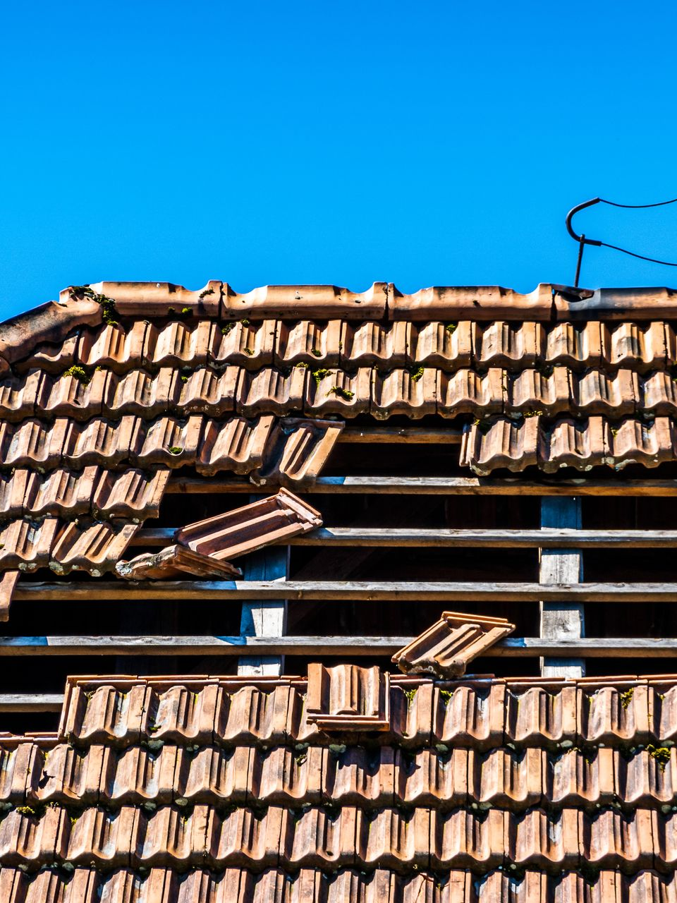 Toiture en tuiles de terre cuite endommagée, avec des tuiles manquantes.