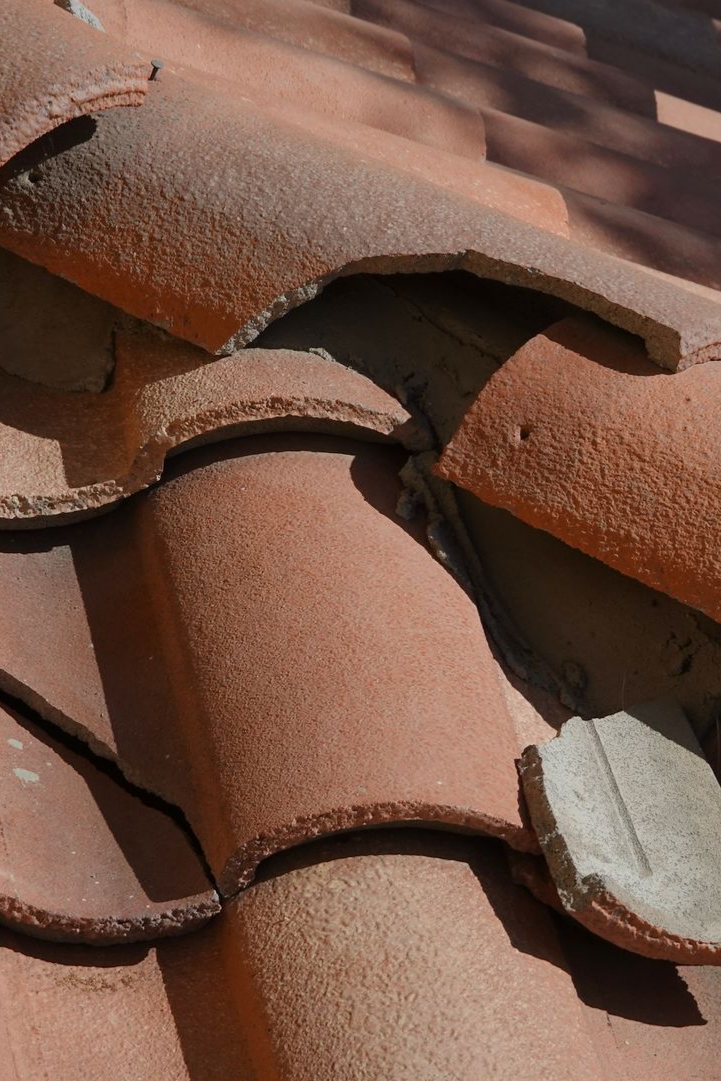 Gros plan sur des tuiles de toit en terre cuite rouge, patinées par le temps.