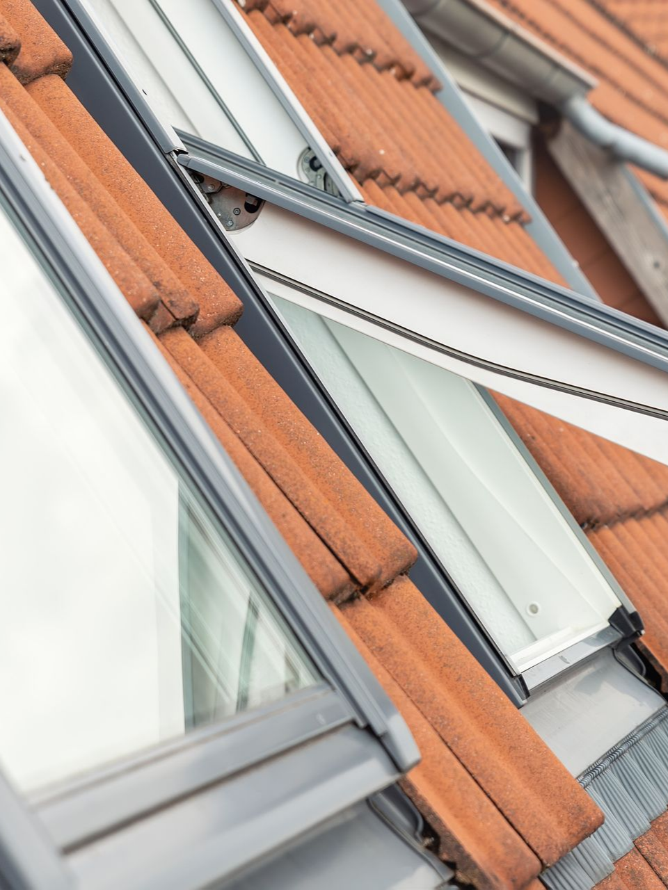 Gros plan sur une lucarne ouverte à cadre blanc sur un toit de tuiles rouges.