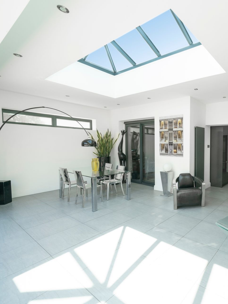 Salle à manger spacieuse avec une grande verrière. Table et chaises en verre, lumière naturelle, murs blancs.