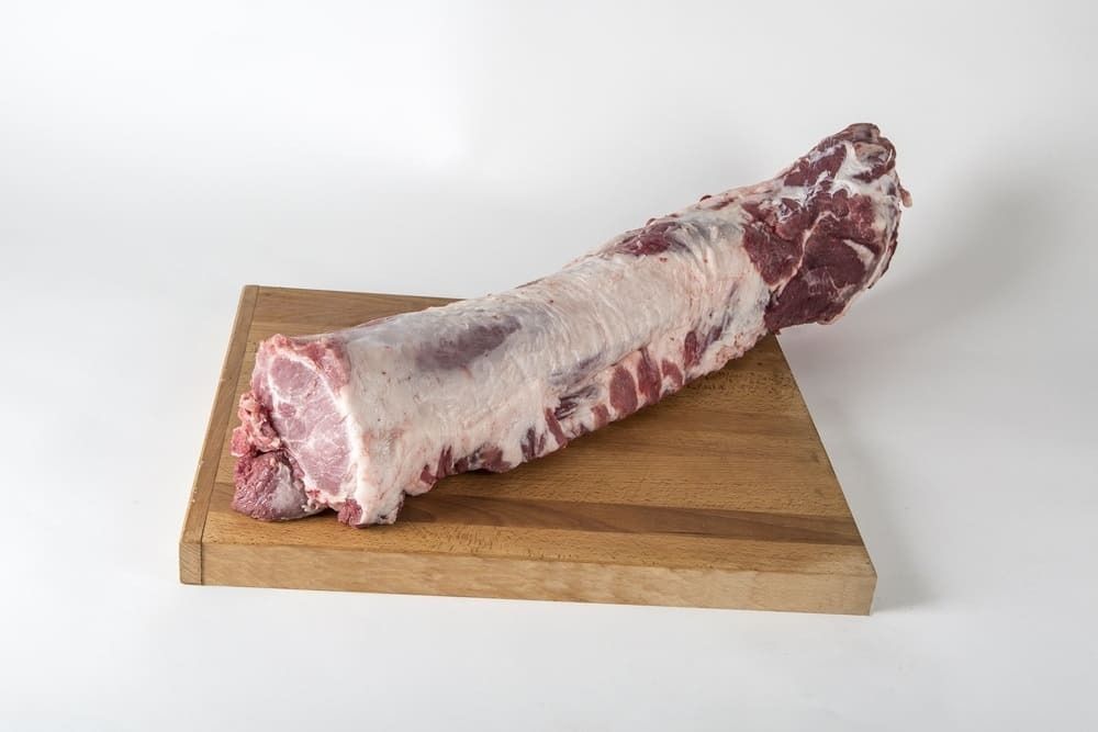 Un trozo de carne cruda reposa encima de una tabla de cortar de madera.