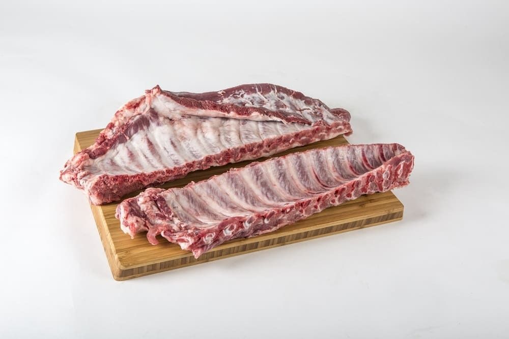 Dos costillas de cerdo crudas están colocadas sobre una tabla de cortar de madera.
