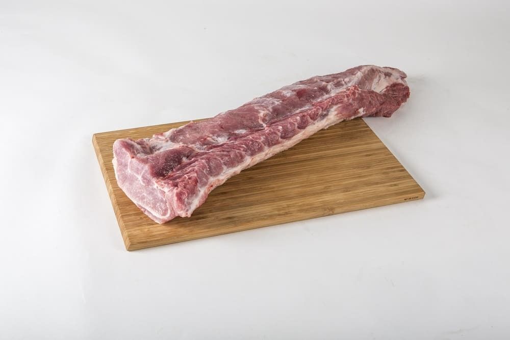 Un trozo de carne cruda reposa encima de una tabla de cortar de madera.