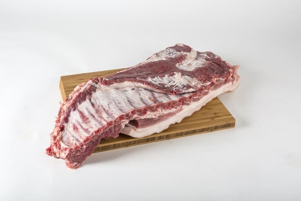 Un trozo de carne cruda reposa encima de una tabla de cortar de madera.