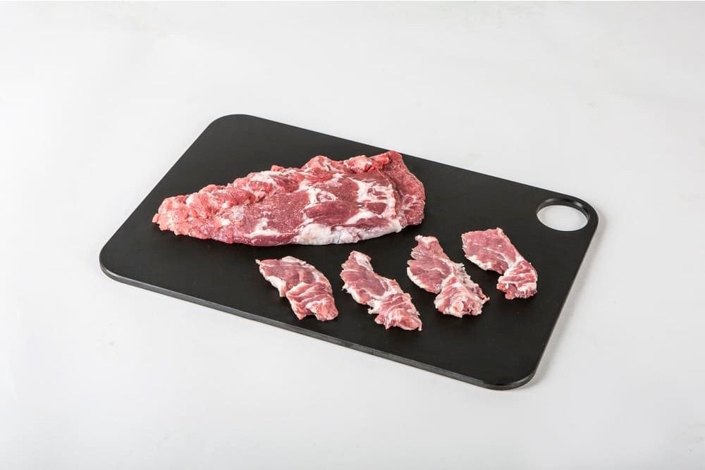 Un trozo de carne reposa sobre una tabla de cortar negra.