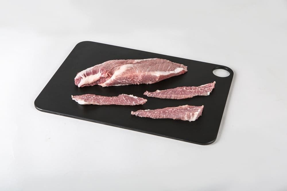 Un trozo de carne reposa sobre una tabla de cortar negra.