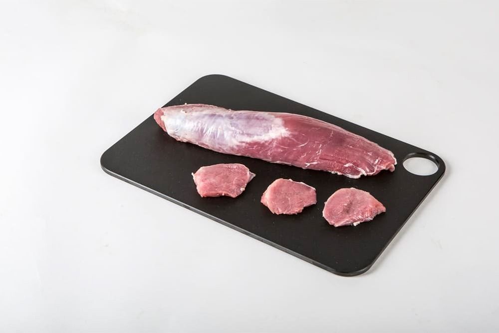 Un trozo de carne reposa sobre una tabla de cortar negra.