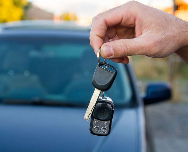 Una persona sostiene una llave de coche delante de un coche.