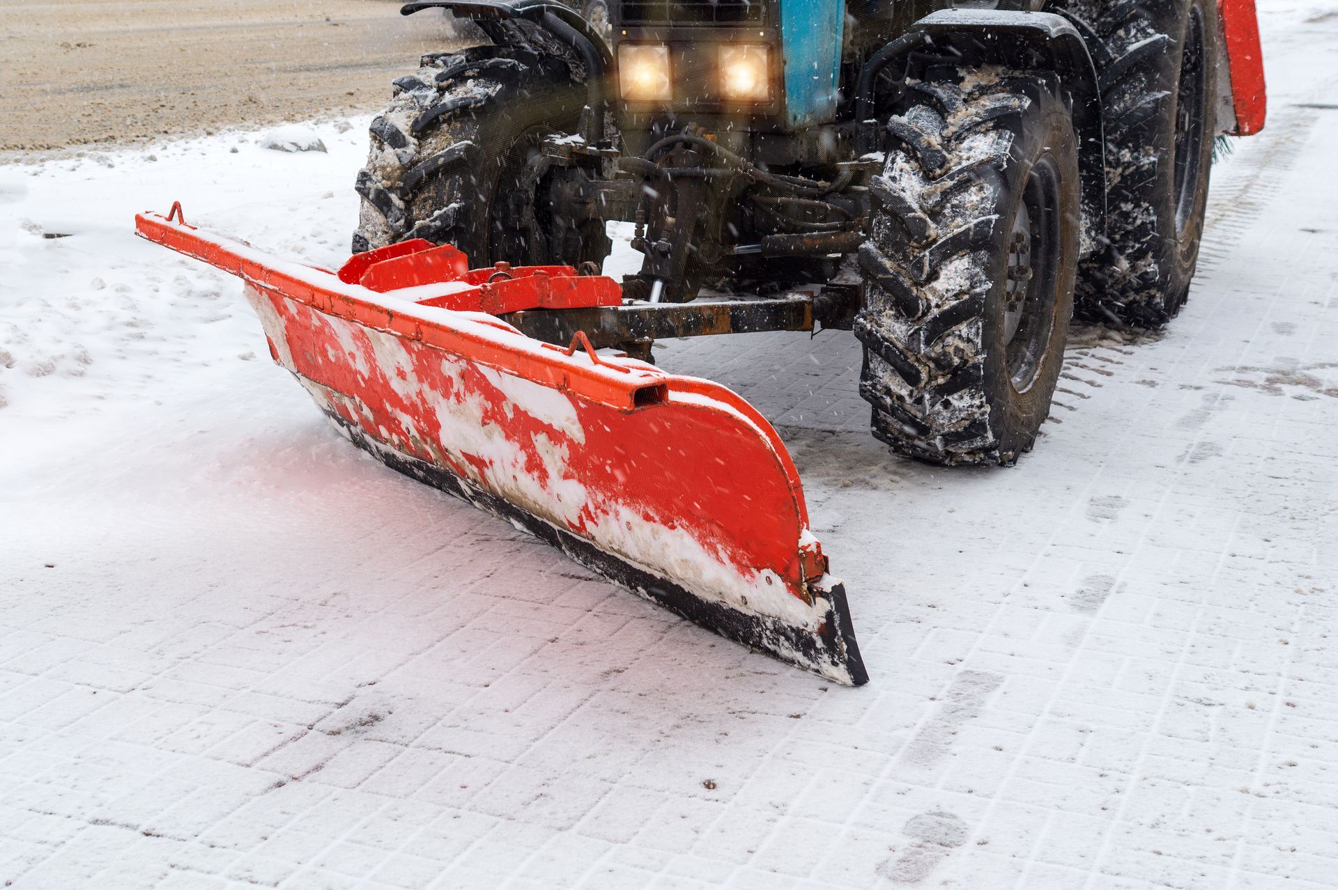 Roter Schneepflug, der an einem Traktor befestigt ist und Schnee von einer gepflasterten Fläche räumt.