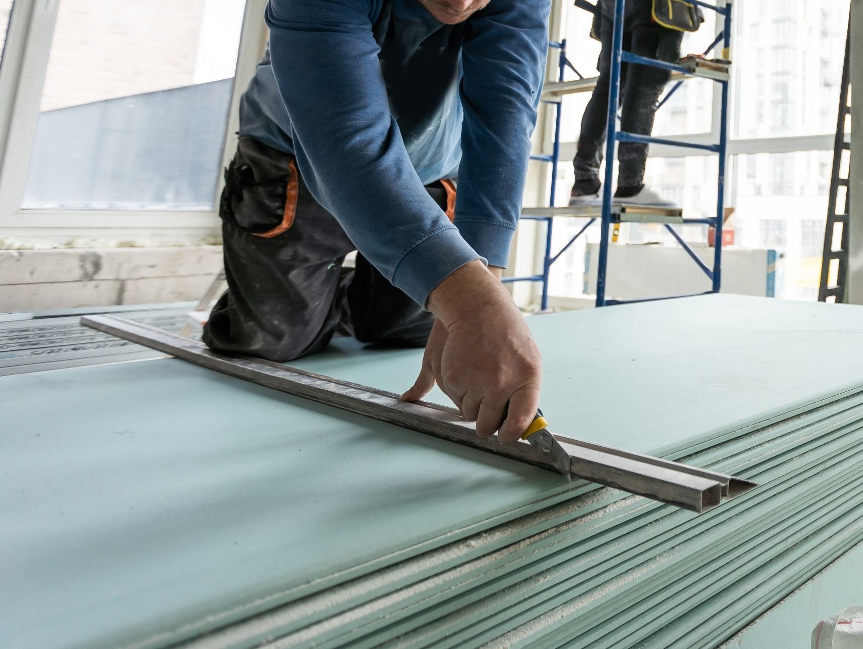 Un hombre está midiendo un trozo de panel de yeso con una cinta métrica.