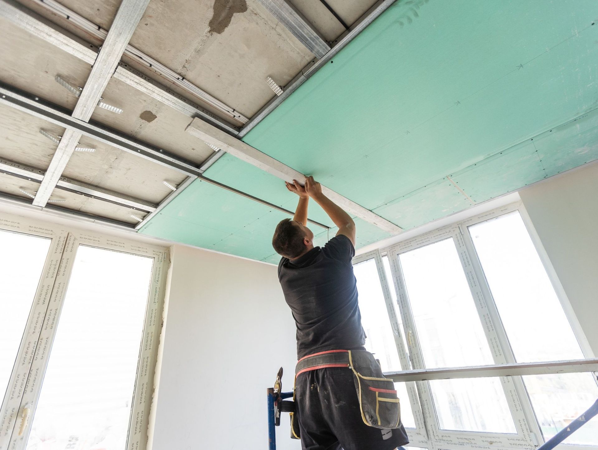Un hombre está trabajando en el techo de una habitación con muchas ventanas.
