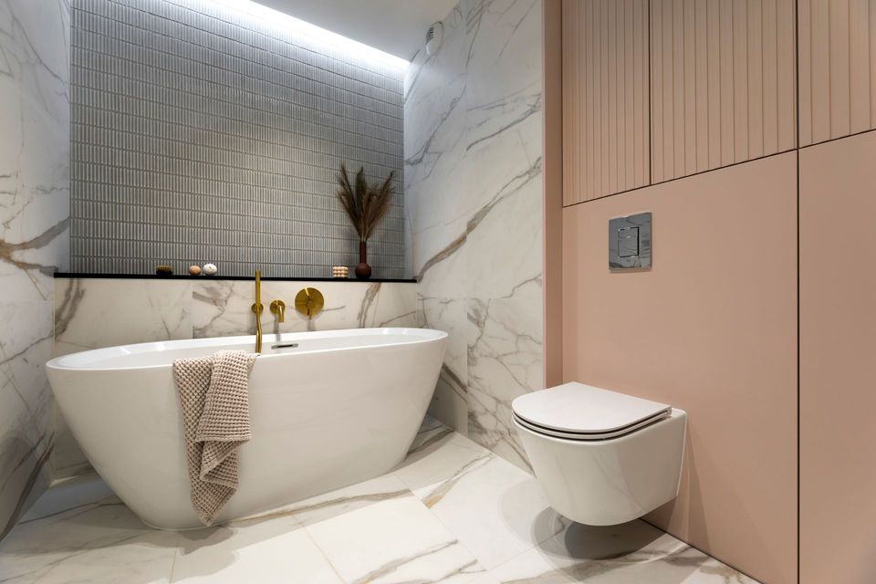Salle de bain moderne avec une baignoire blanche, des murs en marbre et un mur rose à côté d'une toilette flottante.
