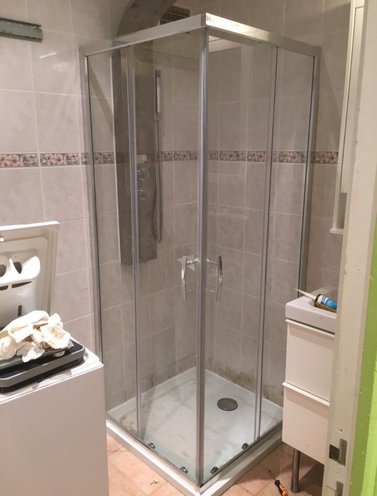 Pièce vide avec murs et sol carrelés dans des tons beiges. Plomberie visible sur le mur et près du sol.