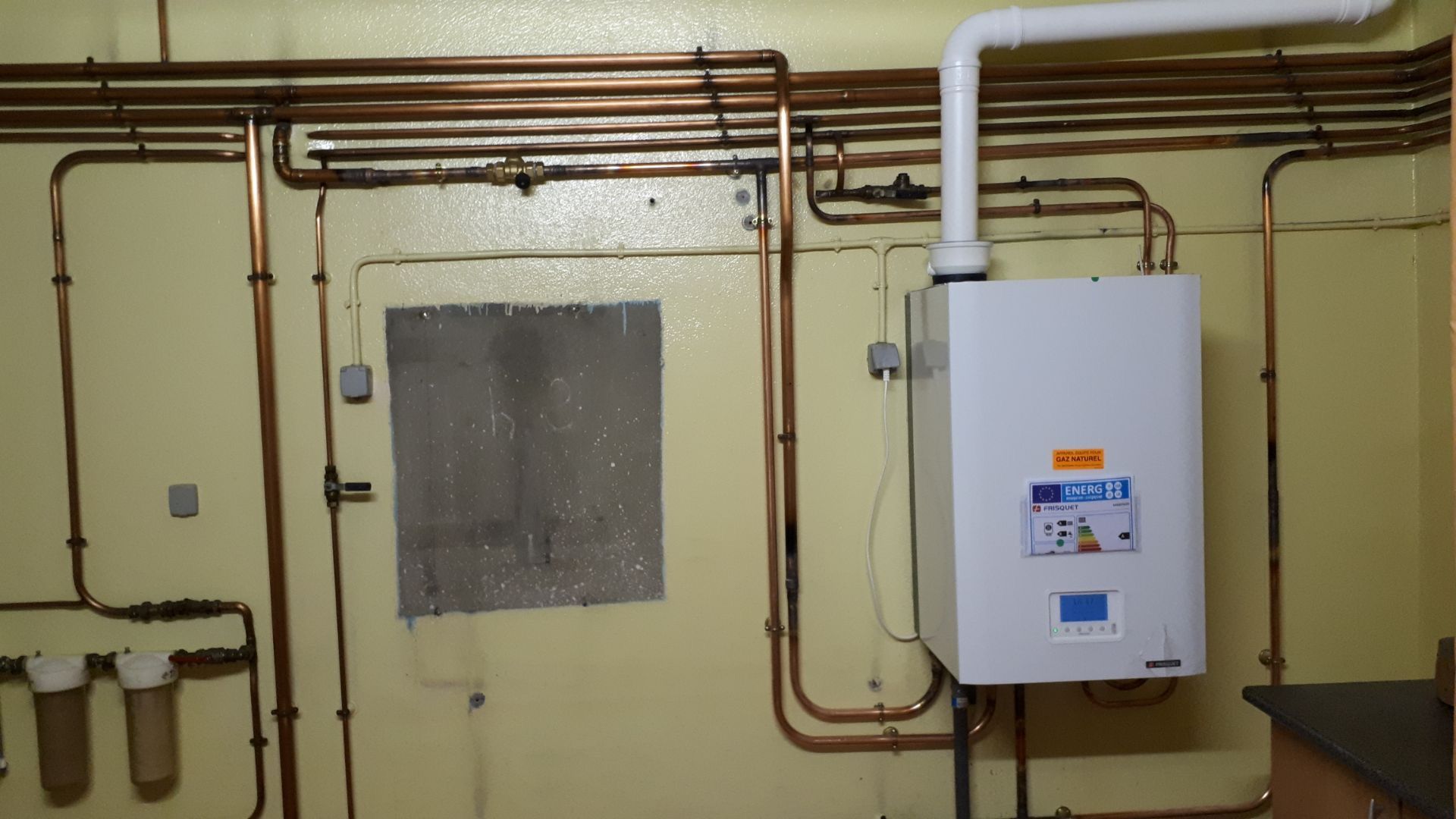 Système de chauffage avec panneaux de contrôle noirs, tuyaux en cuivre et chaudière blanche dans un sous-sol.