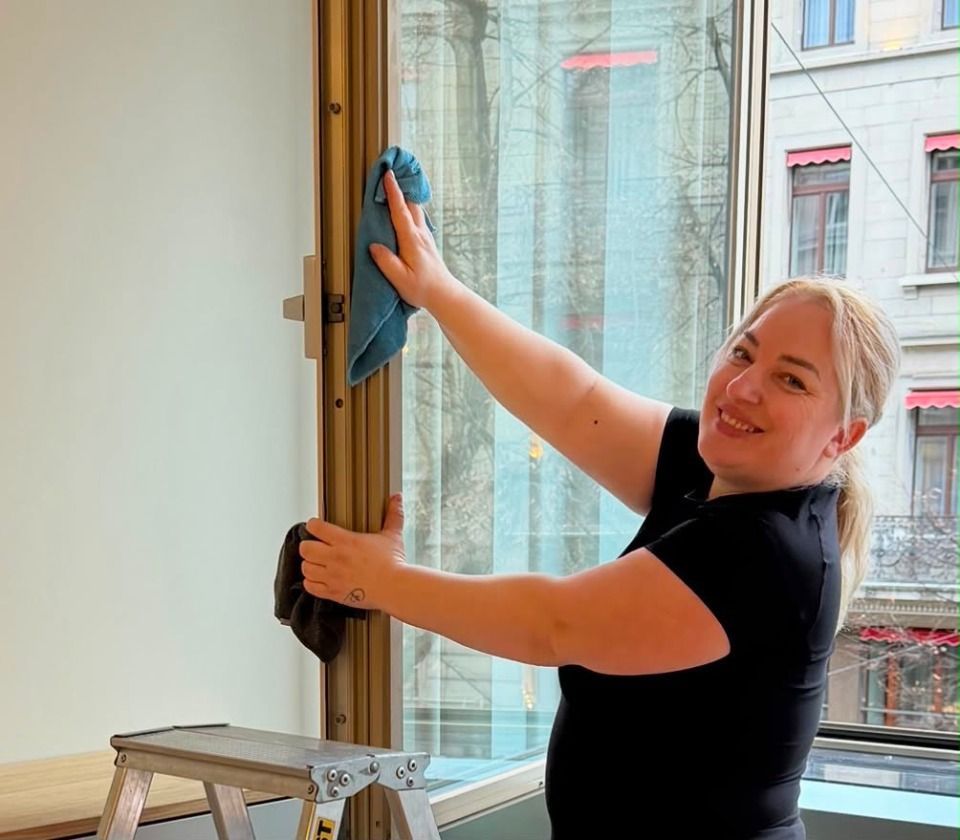 Eine Person saugt einen weissen Teppich in einem hellen Wohnzimmer mit grauem Sofa und gelbem Staubsauger.