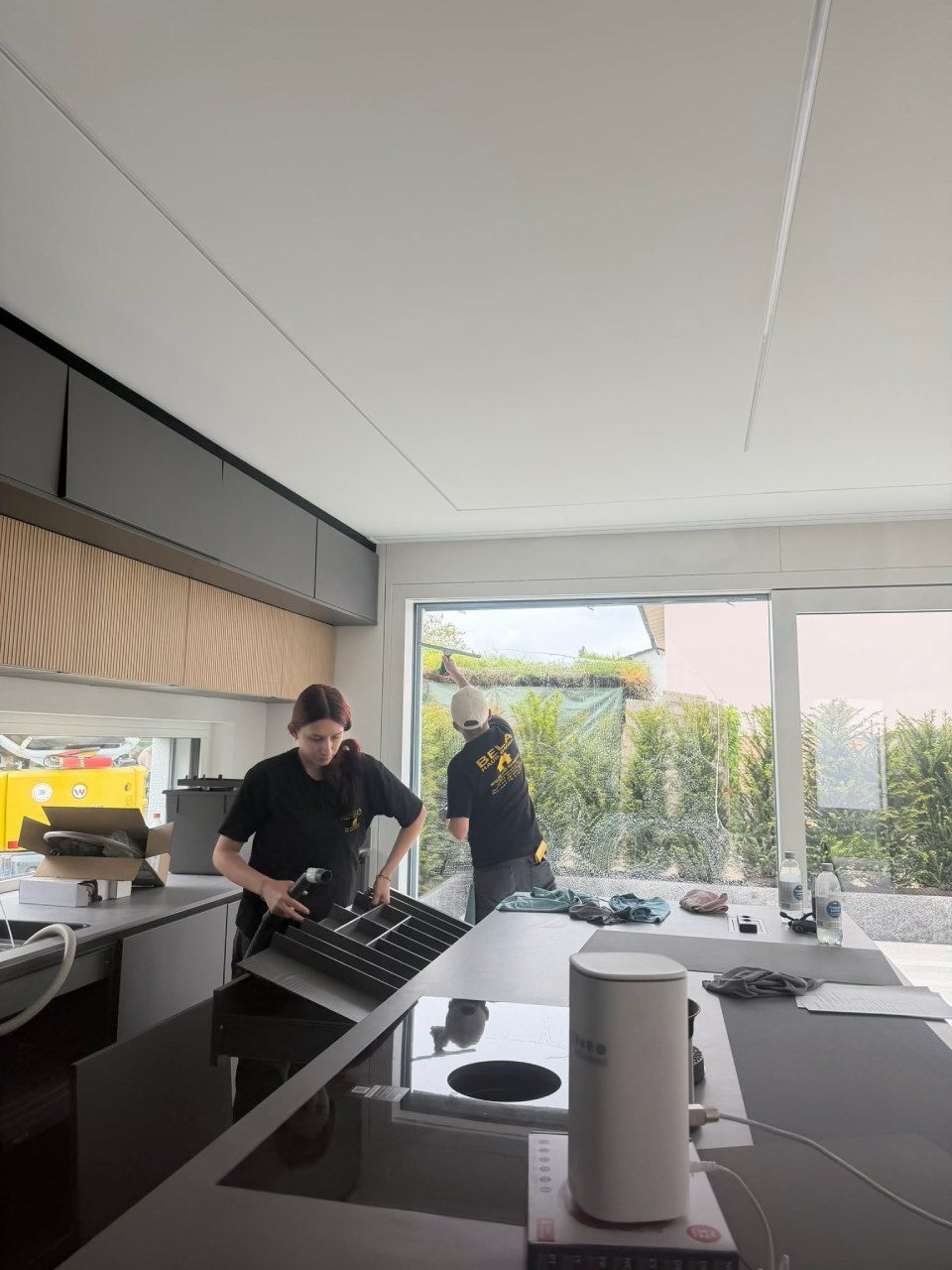 Zwei Personen arbeiten in einer modernen Küche mit grosser Kochinsel und offenen Terrassentüren.
