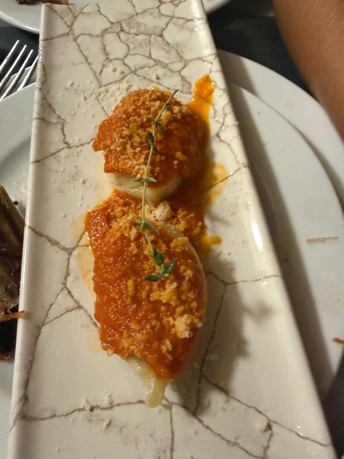 Dos aperitivos empanizados y cubiertos de salsa en un plato blanco con una guarnición verde