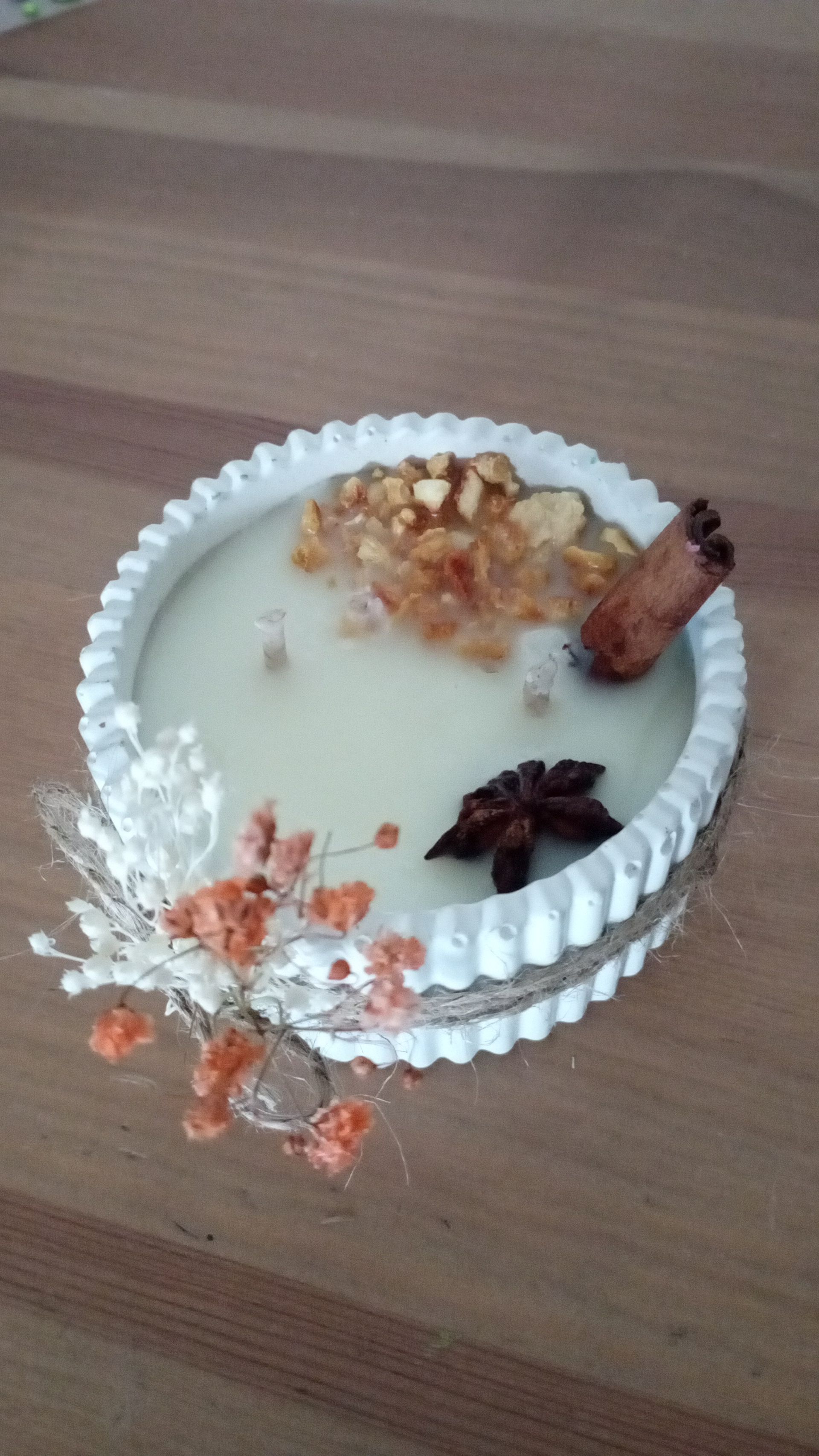 Un pastel blanco con ramas de canela y flores secas sobre una mesa de madera.