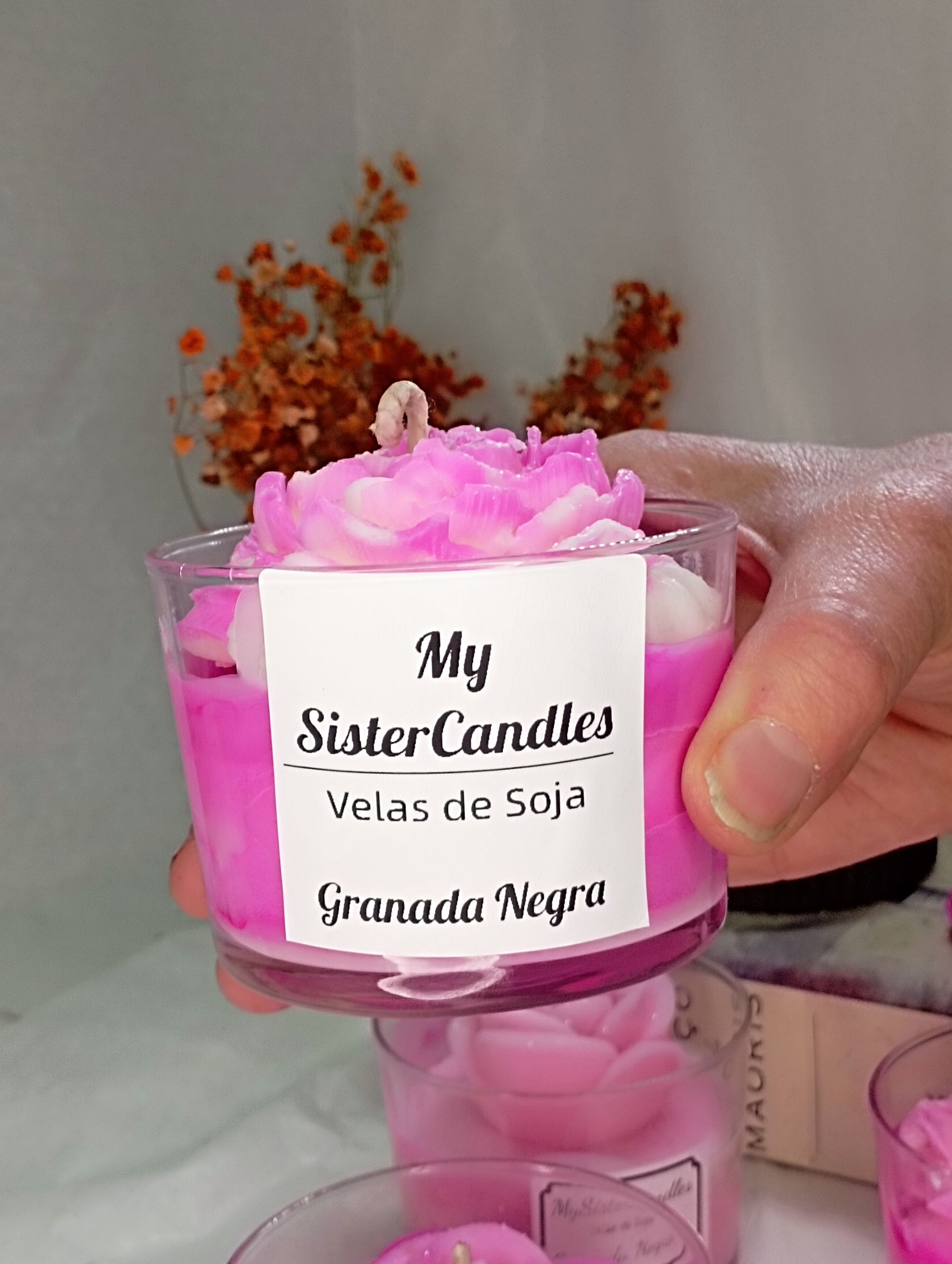 Una persona sostiene una vela rosa en un vaso.