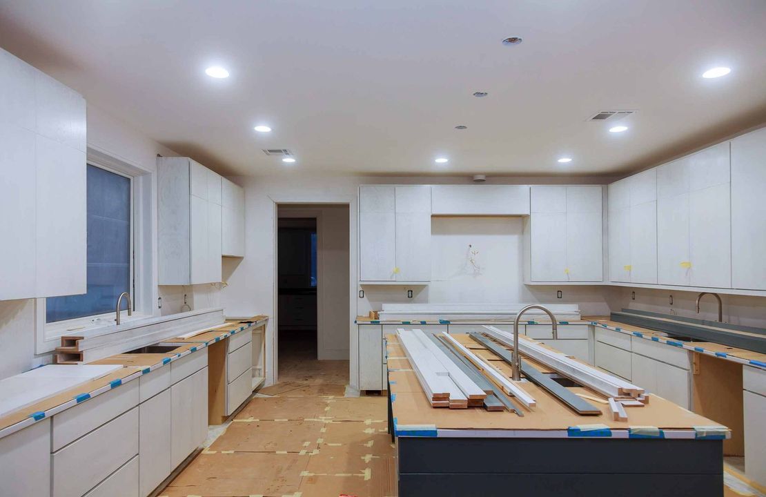 Reforma de cocina en proceso, muebles blancos, isla con fregadero, materiales de construcción, tonos neutros.