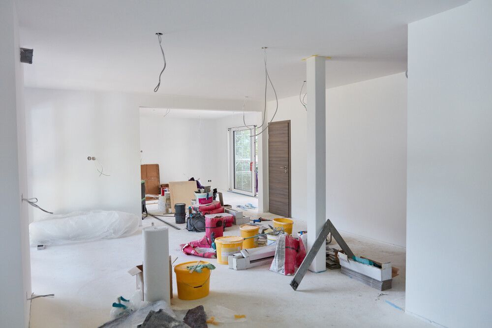 Habitación en construcción con paredes blancas, cableado expuesto y materiales de construcción esparcidos por todas partes.