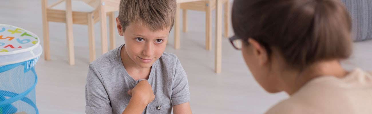 Un niño pequeño está sentado en el suelo hablando con una mujer.