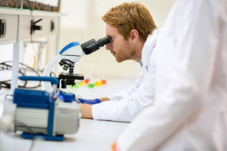 Científico utilizando un microscopio en un laboratorio, con equipo de laboratorio sobre la mesa.