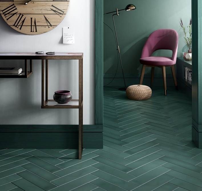 Una habitación verde azulado con suelo de baldosas en espiga. Una silla rosa se encuentra en la entrada, con un reloj y una consola en primer plano.