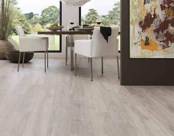 Piso de apariencia de madera clara en un comedor con sillas blancas, una mesa preparada para comer y una gran pintura abstracta.