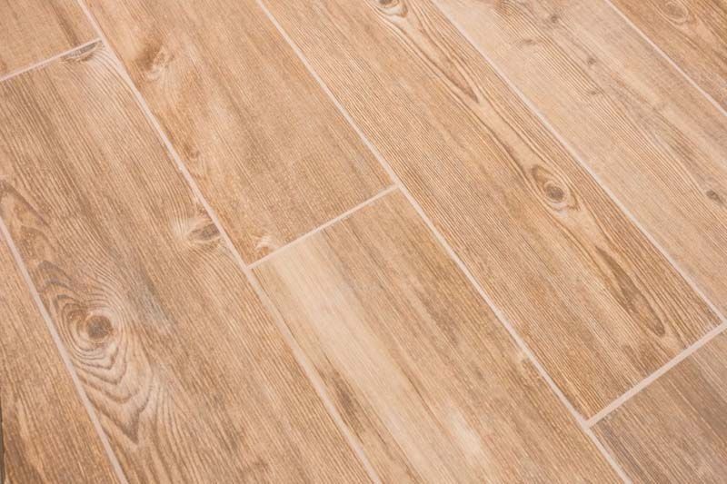 Piso de baldosas de cerámica con apariencia de madera de color marrón claro instalado en un patrón diagonal, con vetas y líneas de lechada visibles.