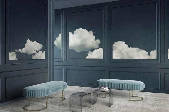 Una habitación serena con paredes revestidas de paneles azules, vinilos de nubes esponjosas y bancos verde azulado. Una pequeña mesa de cristal se encuentra en el centro.