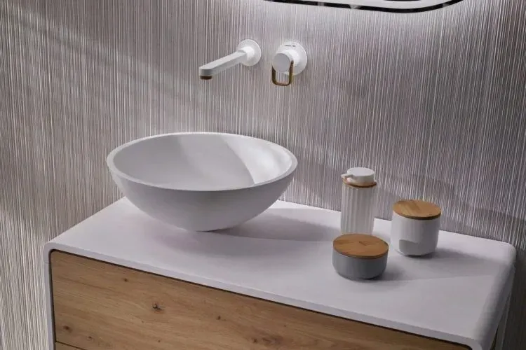 Baño moderno con lavabo blanco, grifo de pared, mueble de tocador de madera y pared texturizada.