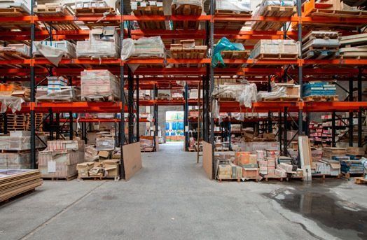 Filas de estanterías repletas de mercancías en un almacén; a lo lejos se ve una carretilla elevadora.