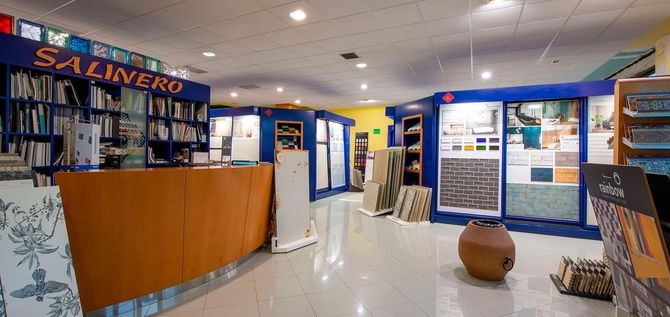 Interior de una tienda con exposición de azulejos y telas. Hay un mostrador de madera curvada y estanterías con materiales.
