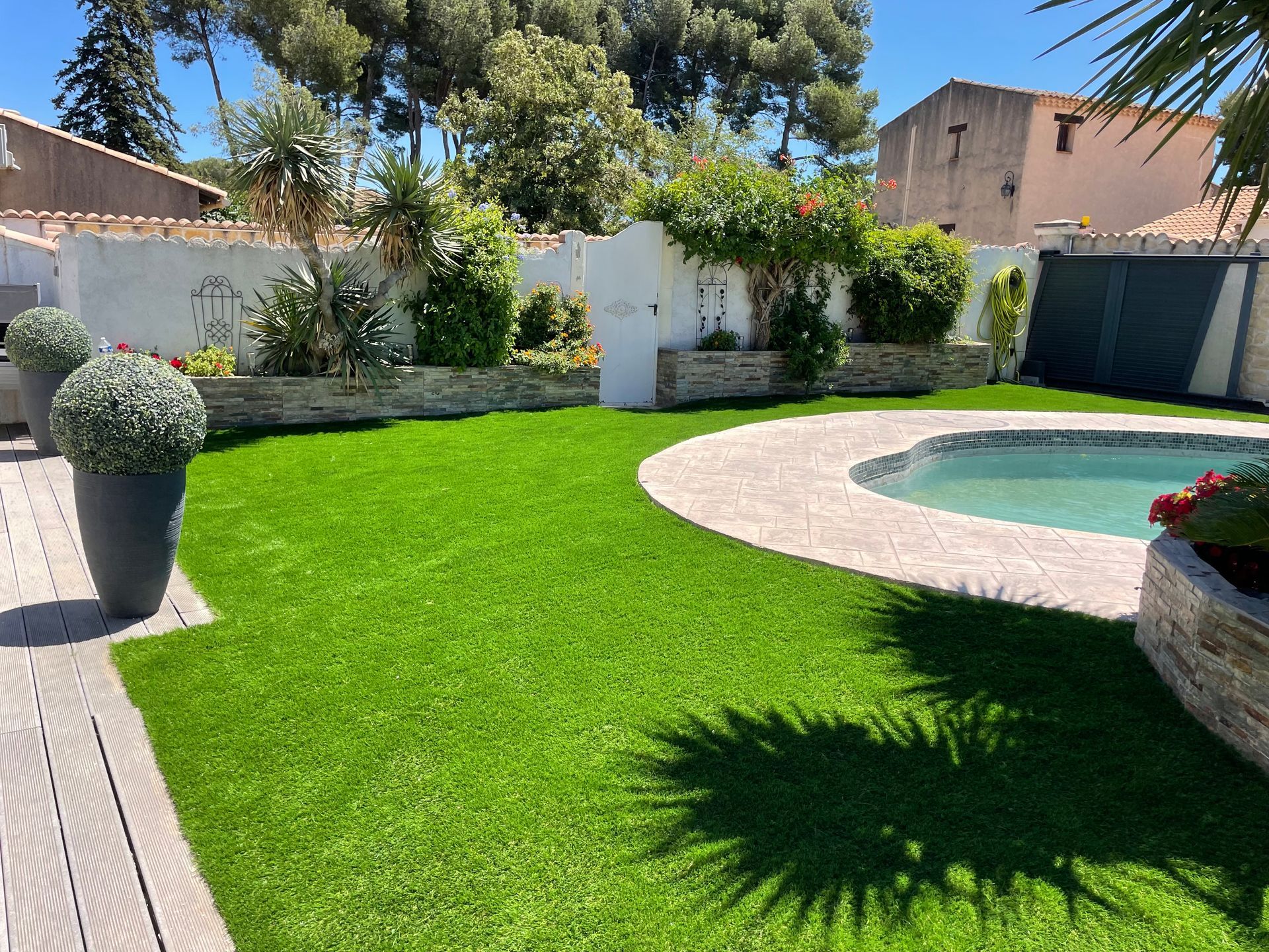 Pelouse artificielle luxuriante avec piscine, allée en pierre et jardinières décoratives dans une cour arrière ensoleillée.
