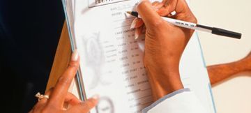 Una persona escribe con un bolígrafo negro en un formulario médico que se puede imprimir en un portapapeles.