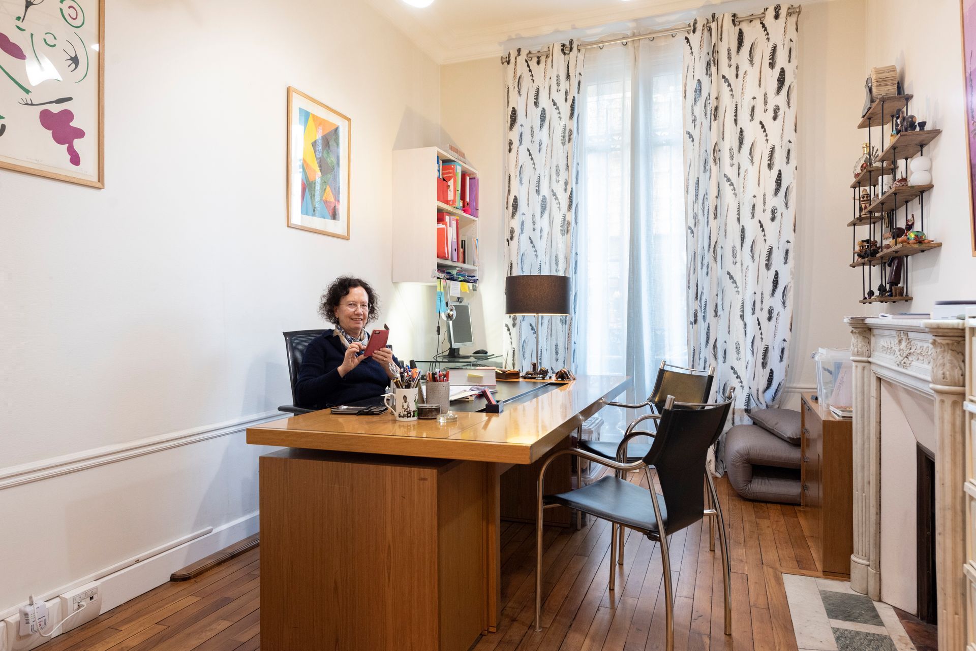 Une personne assise à un bureau en bois dans un bureau à domicile lumineux avec une grande fenêtre et une cheminée.