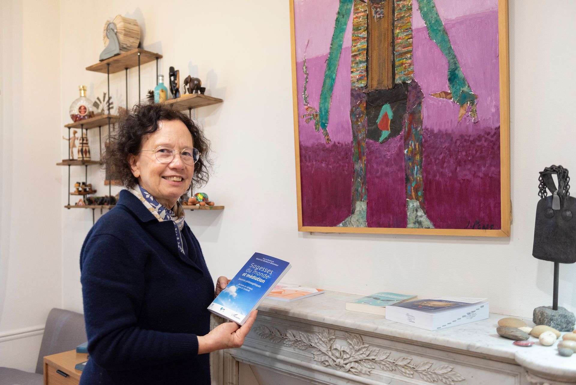 Une personne tenant un livre bleu près d'une cheminée et d'un tableau coloré dans une pièce lumineuse